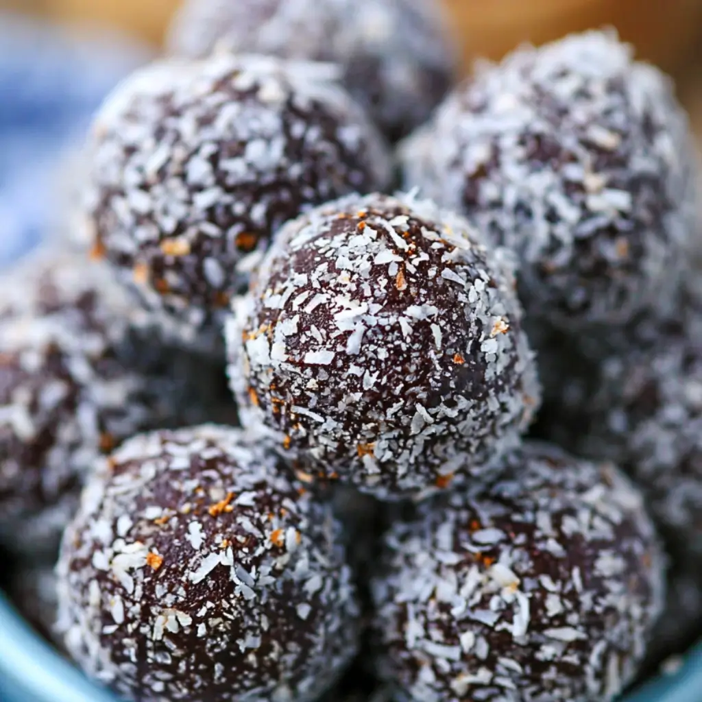 Chocolate coconut protein energy balls coated in shredded coconut and stacked in a bowl